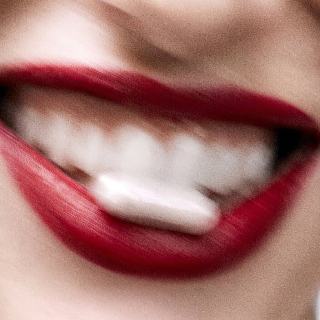 Red lips with a Skin Longevity Complex capsule held between the teeth